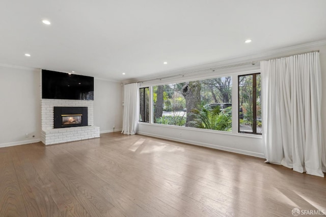 unfurnished living room featuring a brick fireplace, ornamental molding, and light wood-style floors