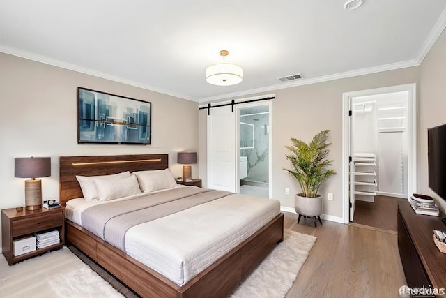 bedroom with a barn door, light wood-style flooring, visible vents, a spacious closet, and crown molding