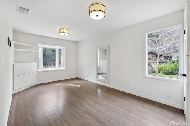 unfurnished room with wood finished floors, visible vents, and baseboards