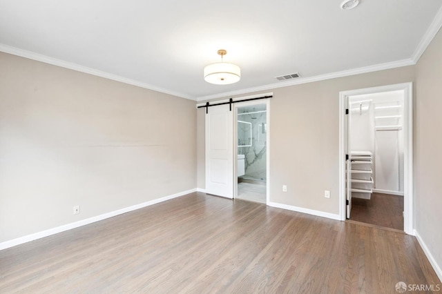 unfurnished bedroom with a barn door, visible vents, wood finished floors, a spacious closet, and crown molding