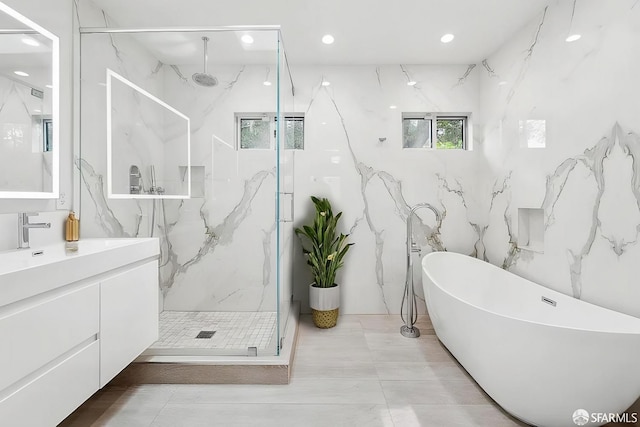 bathroom with recessed lighting, a marble finish shower, a freestanding bath, and vanity