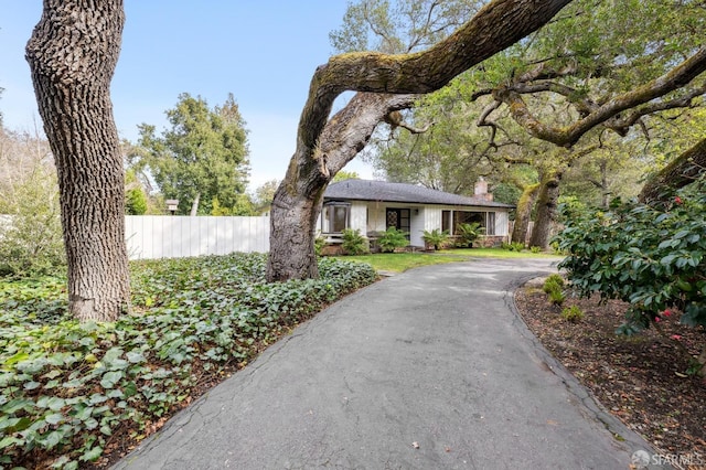 view of front of home featuring driveway, a chimney, and fence