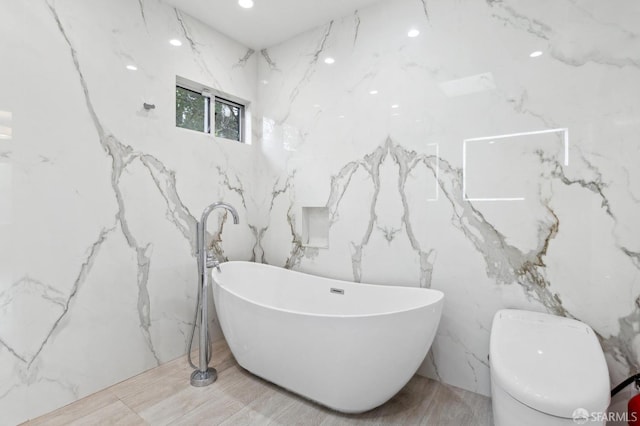 bathroom featuring a freestanding bath, toilet, and stone wall