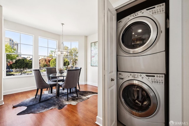 laundry area with plenty of natural light, stacked washer / dryer, hardwood / wood-style floors, and a notable chandelier