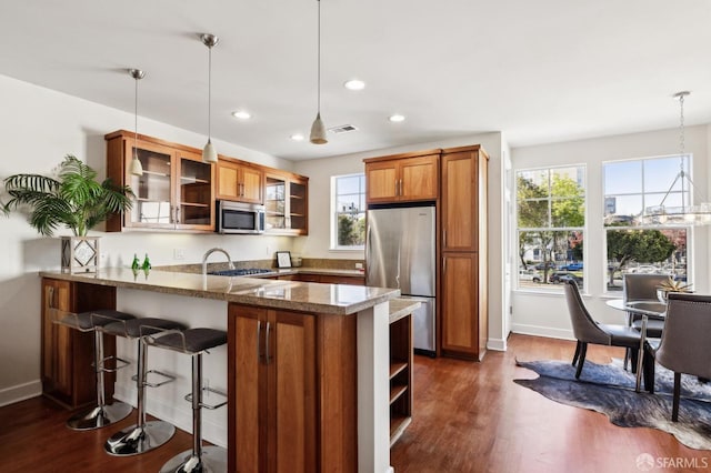 kitchen with stone counters, stainless steel appliances, kitchen peninsula, and decorative light fixtures