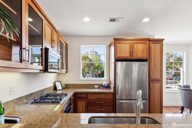 kitchen with sink, light stone countertops, appliances with stainless steel finishes, and plenty of natural light