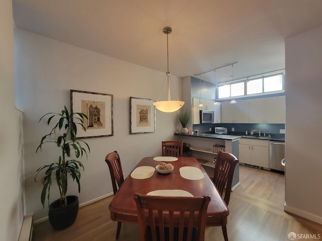 dining area with light wood-type flooring, rail lighting, a baseboard radiator, and sink