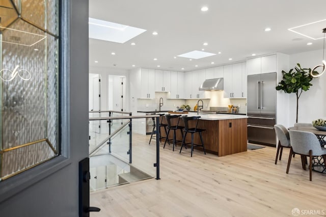 kitchen with stainless steel built in fridge, white cabinets, a kitchen bar, and an island with sink