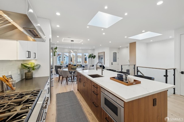 kitchen featuring white cabinetry, stainless steel microwave, island range hood, and an island with sink