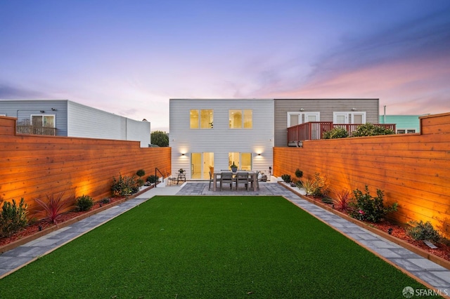 back house at dusk featuring a lawn and a patio