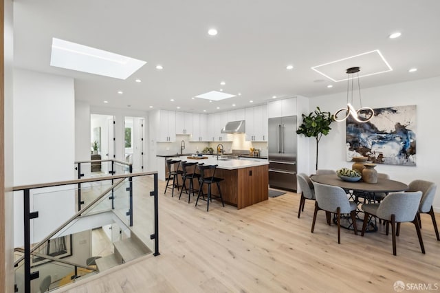 kitchen featuring a kitchen island, white cabinetry, stainless steel built in refrigerator, hanging light fixtures, and a breakfast bar area