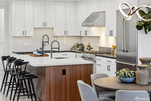 kitchen featuring sink, extractor fan, high end appliances, a center island with sink, and decorative backsplash