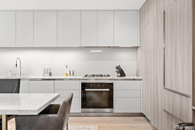 kitchen featuring a sink, black oven, modern cabinets, and white cabinets