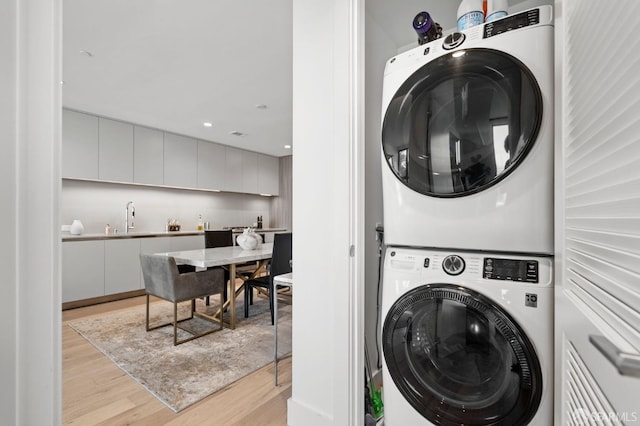 washroom featuring laundry area, stacked washer and dryer, light wood-style floors, and a sink