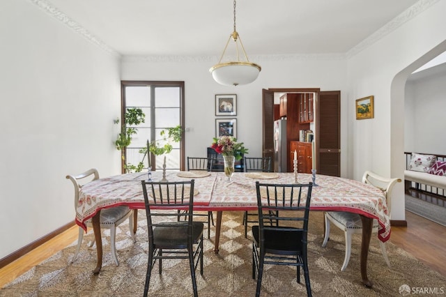 dining room with baseboards, crown molding, arched walkways, and wood finished floors