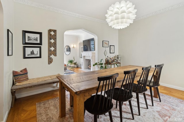 dining area featuring baseboards, arched walkways, a fireplace with flush hearth, crown molding, and a chandelier