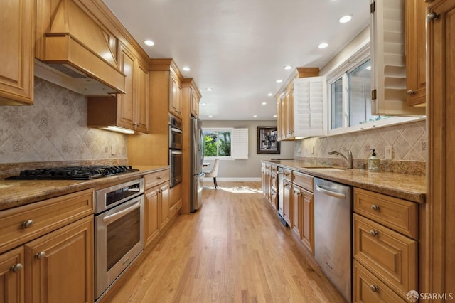 kitchen with premium range hood, appliances with stainless steel finishes, light stone counters, and light hardwood / wood-style flooring