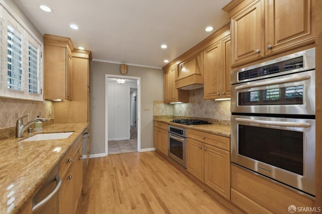 kitchen featuring premium range hood, sink, light stone counters, light hardwood / wood-style flooring, and appliances with stainless steel finishes