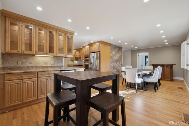 kitchen with light stone counters, stainless steel fridge, backsplash, and light hardwood / wood-style flooring