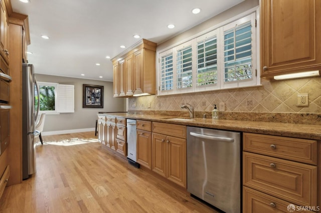 kitchen featuring appliances with stainless steel finishes, tasteful backsplash, sink, light stone countertops, and light hardwood / wood-style flooring