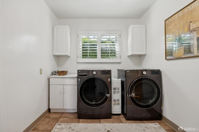 clothes washing area with cabinets, washing machine and clothes dryer, and light tile patterned floors