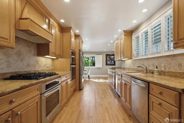 kitchen featuring premium range hood, appliances with stainless steel finishes, sink, light hardwood / wood-style floors, and light stone countertops