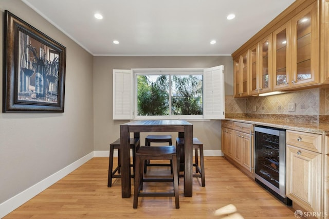 kitchen with beverage cooler, backsplash, crown molding, light stone countertops, and light wood-type flooring