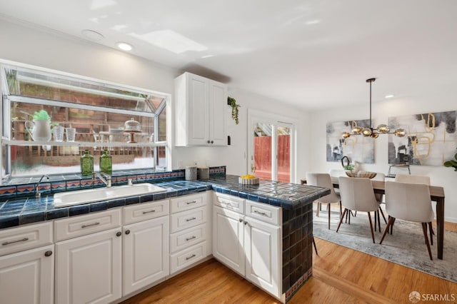 kitchen with a peninsula, light wood-style flooring, white cabinets, and a sink