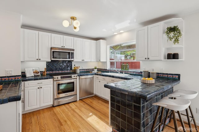 kitchen with appliances with stainless steel finishes, white cabinetry, a sink, and a peninsula