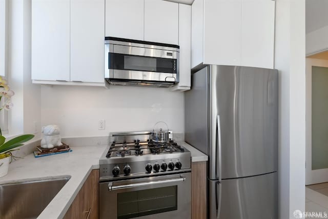 kitchen with appliances with stainless steel finishes, light stone countertops, sink, and white cabinets