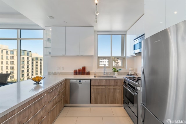 kitchen featuring appliances with stainless steel finishes, sink, light tile patterned floors, and white cabinets