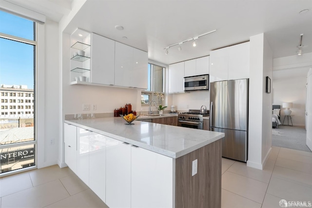 kitchen featuring appliances with stainless steel finishes, light stone countertops, white cabinets, light tile patterned flooring, and kitchen peninsula