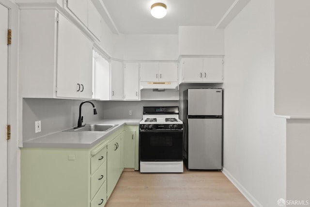 kitchen featuring gas range, freestanding refrigerator, light countertops, under cabinet range hood, and a sink