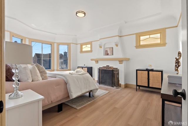 bedroom with a fireplace, baseboards, and wood finished floors