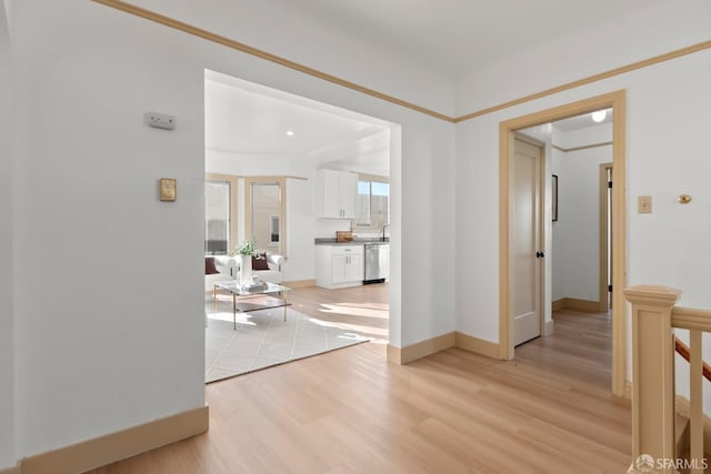 hallway featuring light wood finished floors, a sink, and baseboards