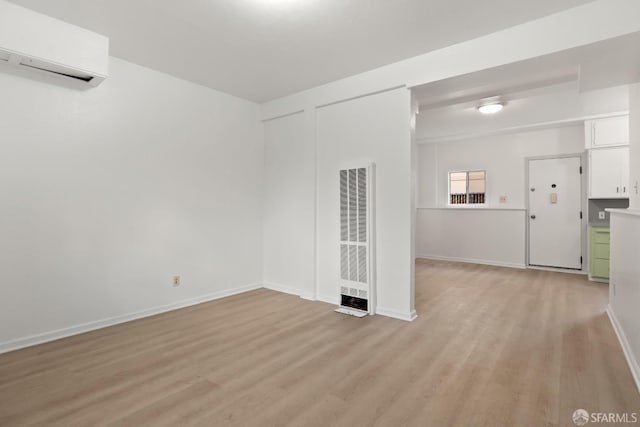 empty room with baseboards, a wall unit AC, and light wood-style floors