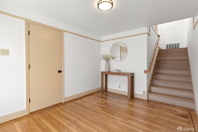 foyer entrance with light wood-type flooring, baseboards, stairs, and visible vents