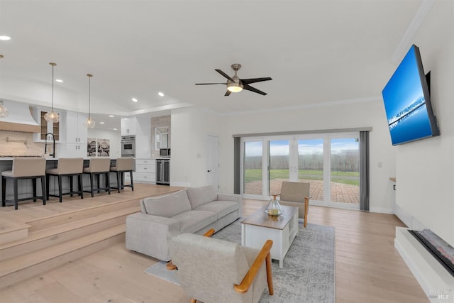 living room with ceiling fan, crown molding, light hardwood / wood-style floors, and sink