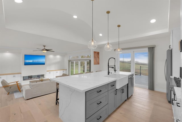 kitchen featuring appliances with stainless steel finishes, an island with sink, ceiling fan, hanging light fixtures, and light stone counters