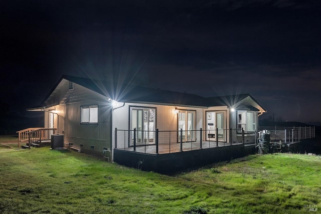 back house at night with cooling unit, a lawn, and french doors