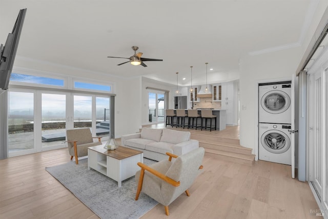 living room with ceiling fan, stacked washer and dryer, crown molding, and light hardwood / wood-style flooring