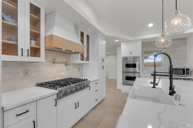 kitchen featuring pendant lighting, custom exhaust hood, white cabinetry, appliances with stainless steel finishes, and light stone counters