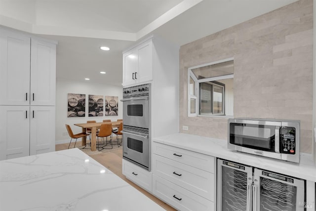 kitchen featuring light stone countertops, beverage cooler, white cabinetry, stainless steel appliances, and light hardwood / wood-style floors