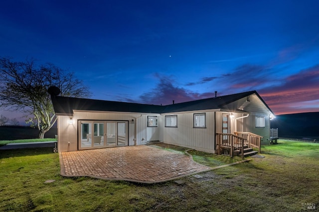 back house at dusk featuring a lawn and a patio