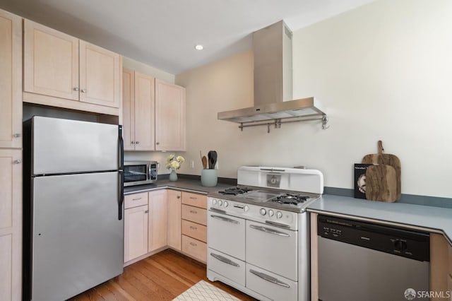 kitchen with light brown cabinets, stainless steel appliances, wall chimney exhaust hood, and light hardwood / wood-style floors