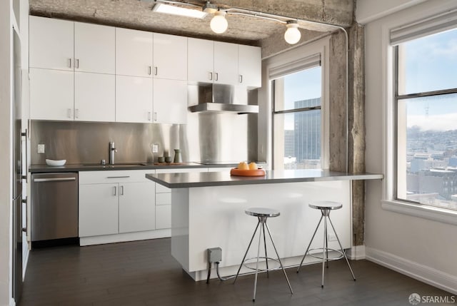 kitchen featuring wall chimney exhaust hood, white cabinets, dishwasher, and kitchen peninsula