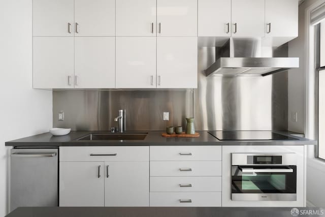 kitchen featuring wall chimney exhaust hood, white cabinets, appliances with stainless steel finishes, and sink