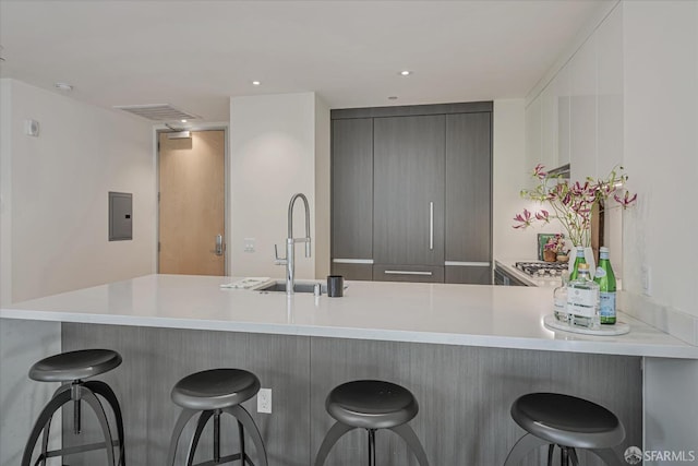 kitchen with kitchen peninsula, gray cabinetry, a breakfast bar, sink, and electric panel