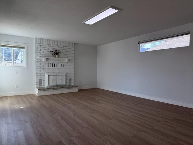 unfurnished living room featuring a healthy amount of sunlight, a brick fireplace, baseboards, and dark wood finished floors