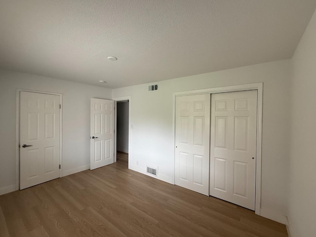 unfurnished bedroom with a closet, visible vents, baseboards, and wood finished floors